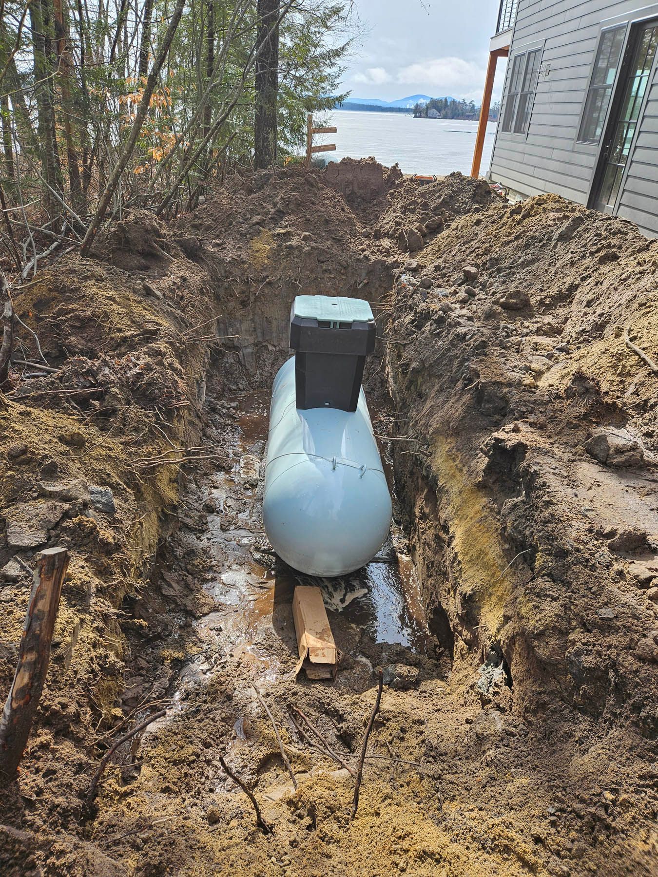 A propane tank in a trench. It is next to a building and a body of water.