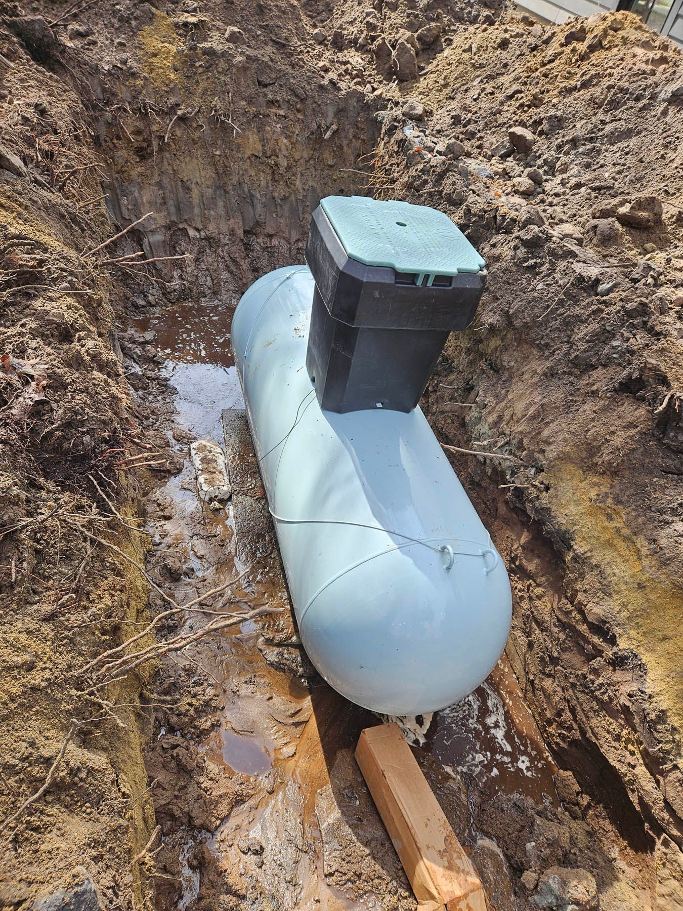 A propane tank in a trench, next to a control box, in a dirt setting.