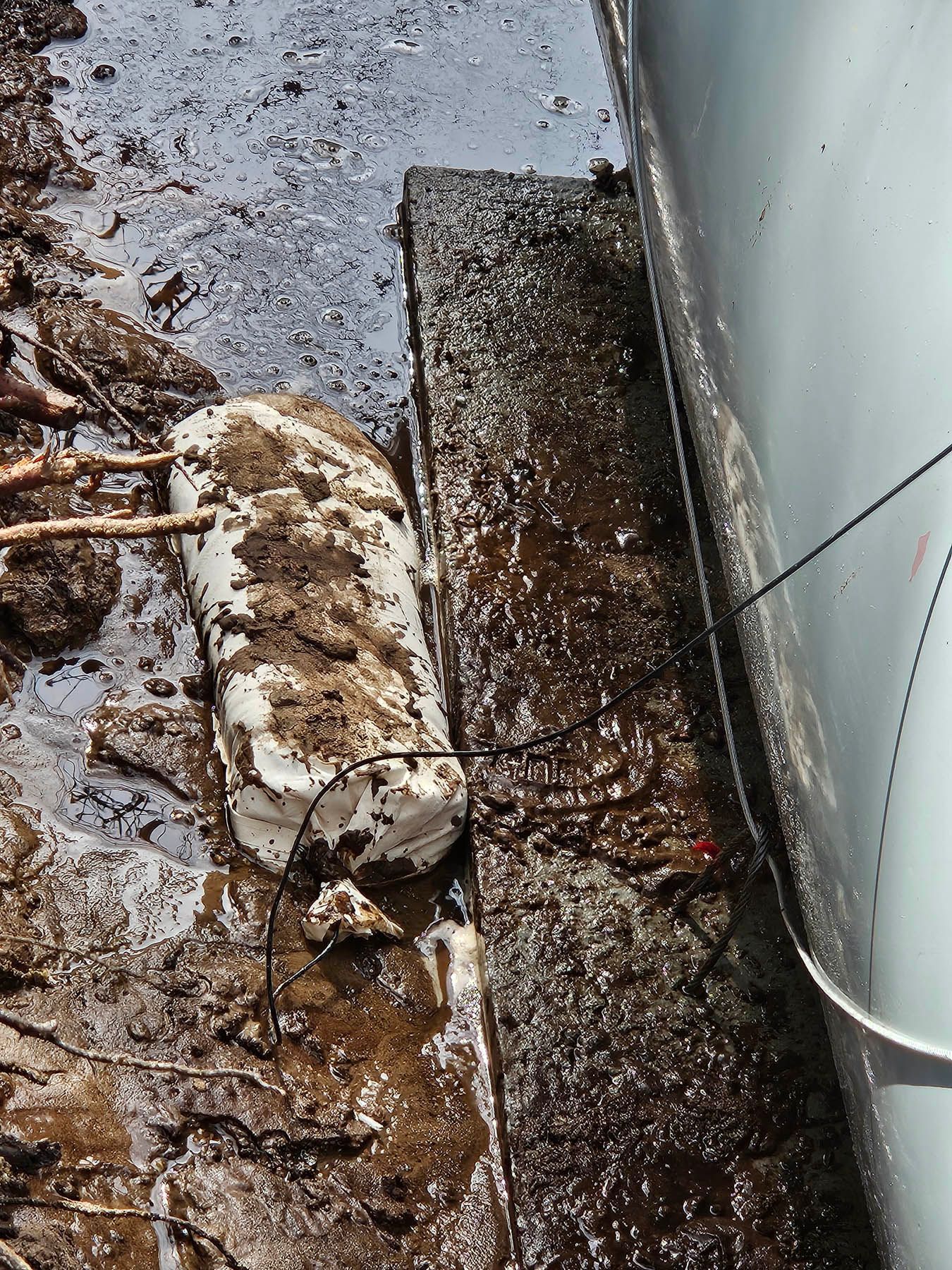 Mud-covered object next to a structure, with visible cables and wires.