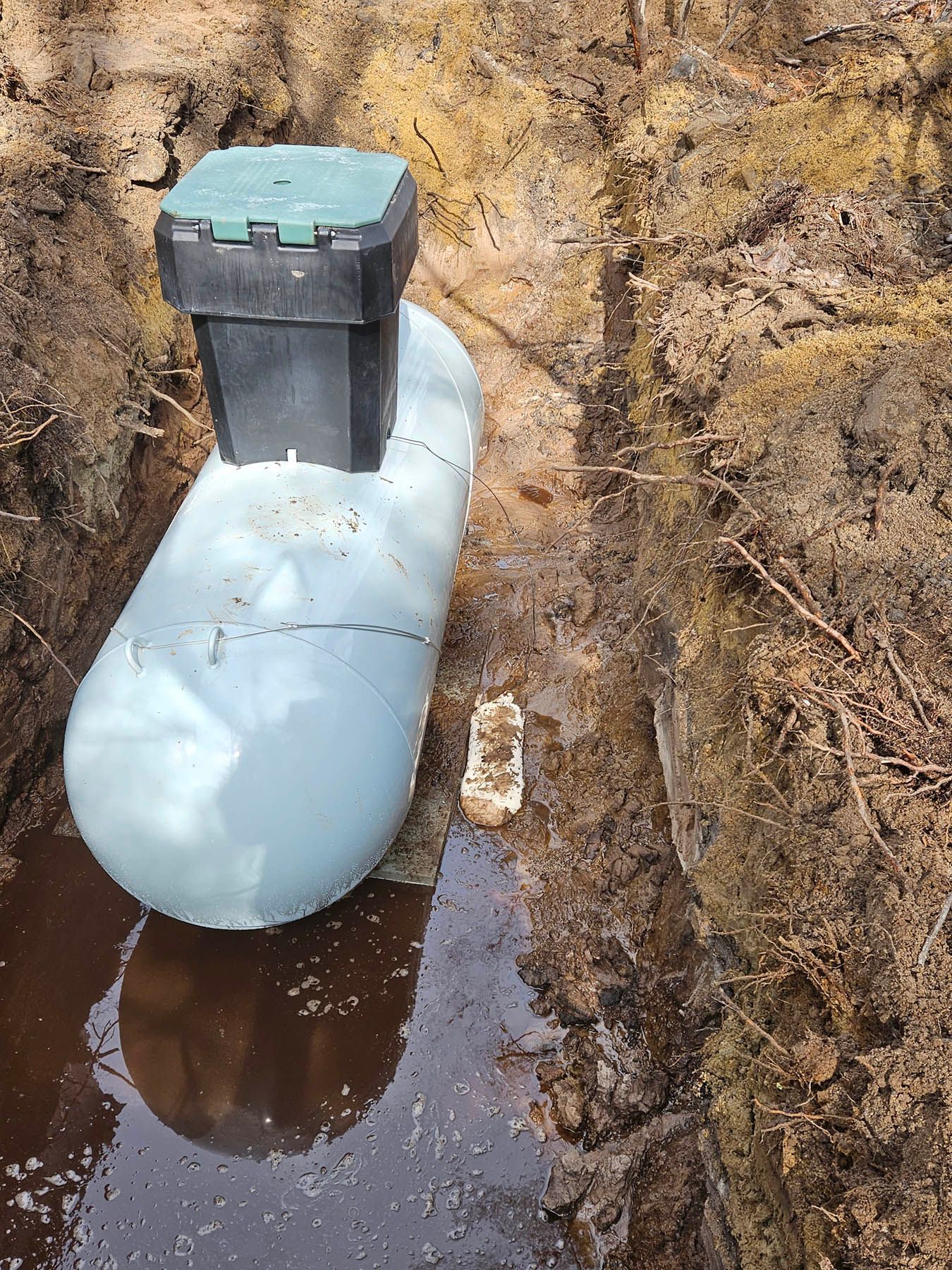 A propane tank in a muddy trench, with a green and black lid.