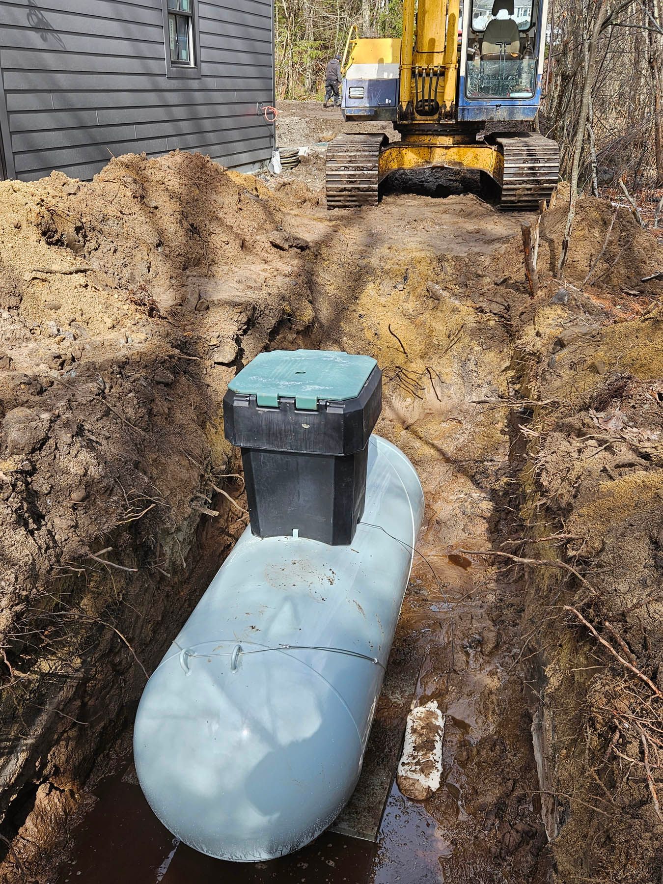 A propane tank is installed in a trench, with an excavator in the background.