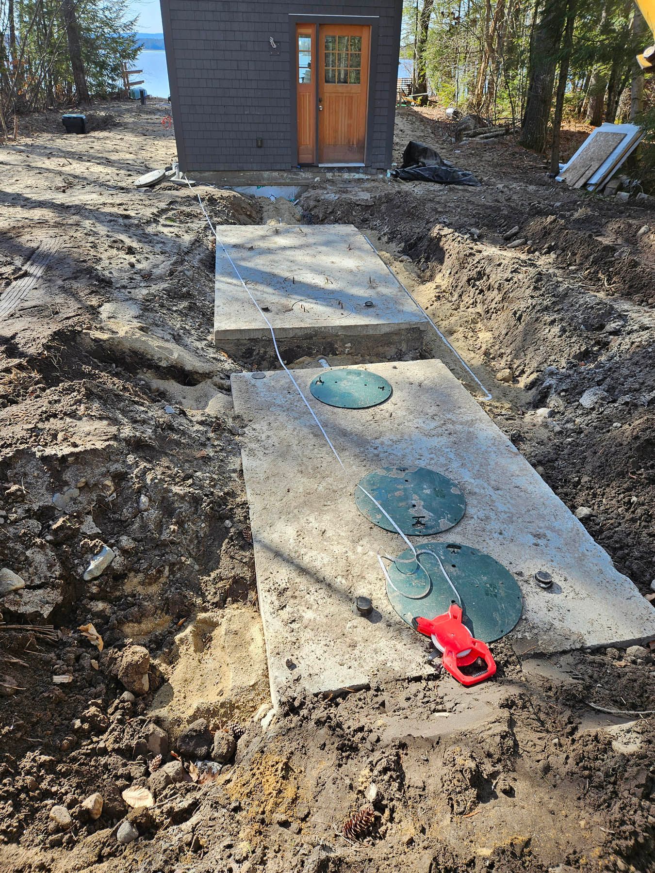 Septic tank installation in progress. Three green lids sit on a concrete slab near a brown cabin.