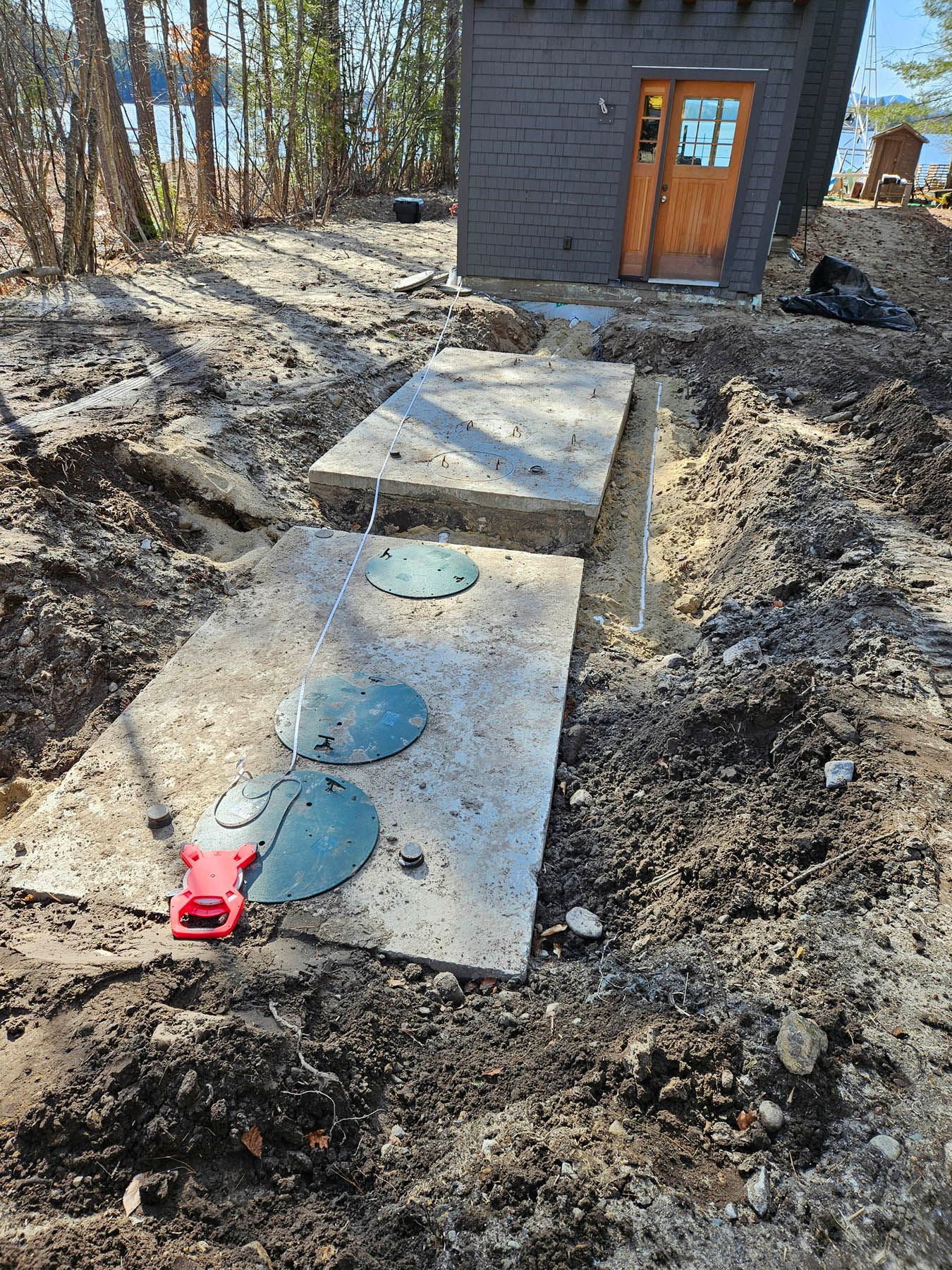 Concrete septic tank covers installed near a brown building, surrounded by dirt and trees.