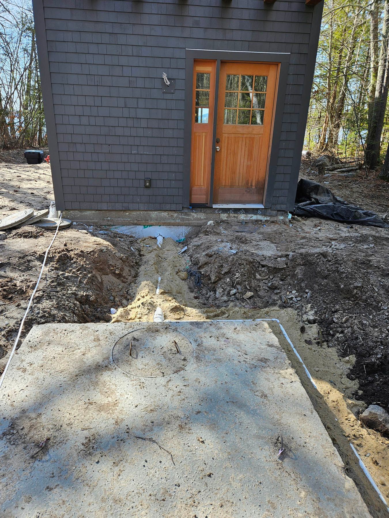Exterior view of a wooden door set into a dark brick building, leading to a concrete pathway in a dirt area.