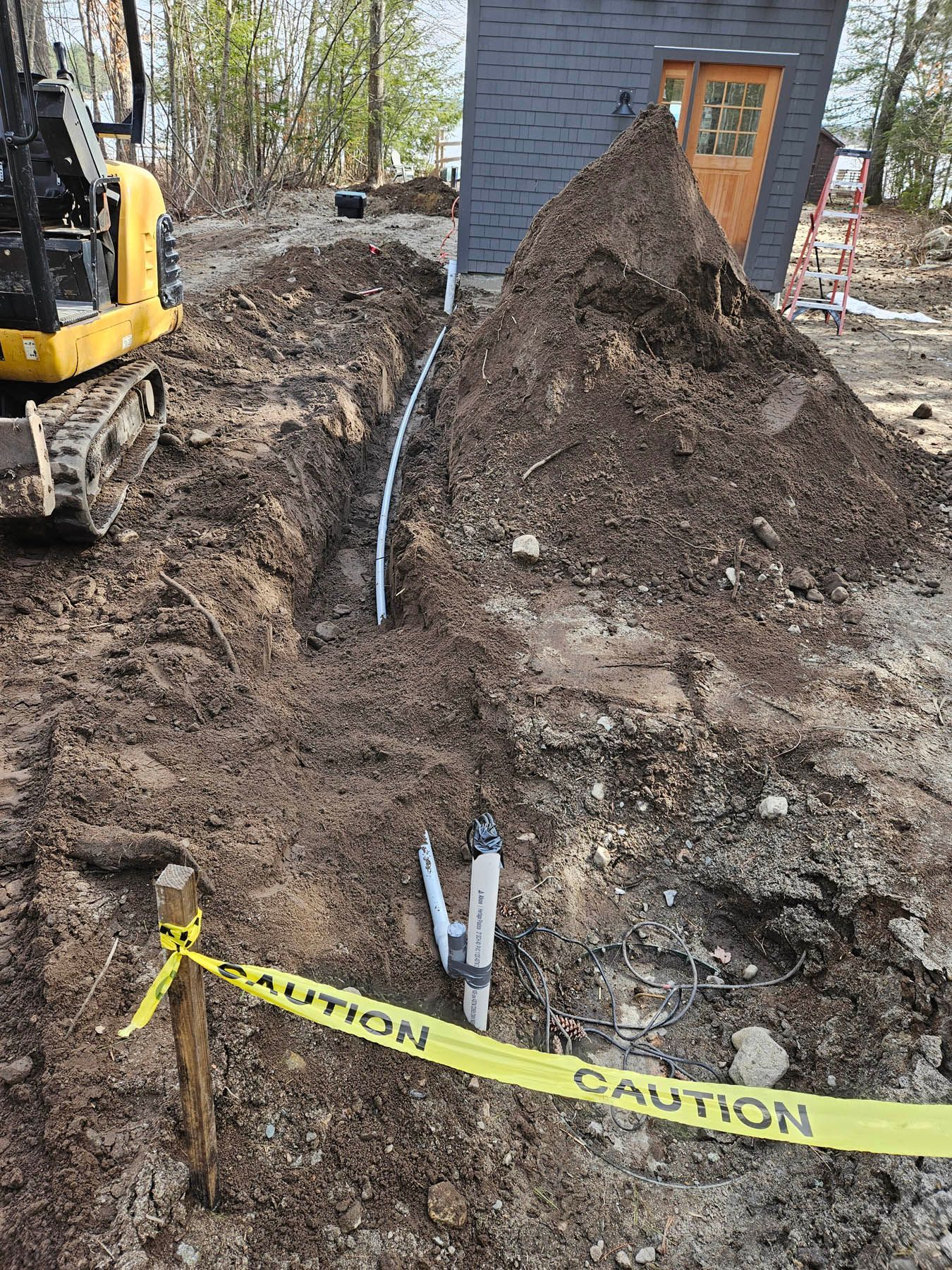 A construction site with a trench, warning tape, and a mini excavator.