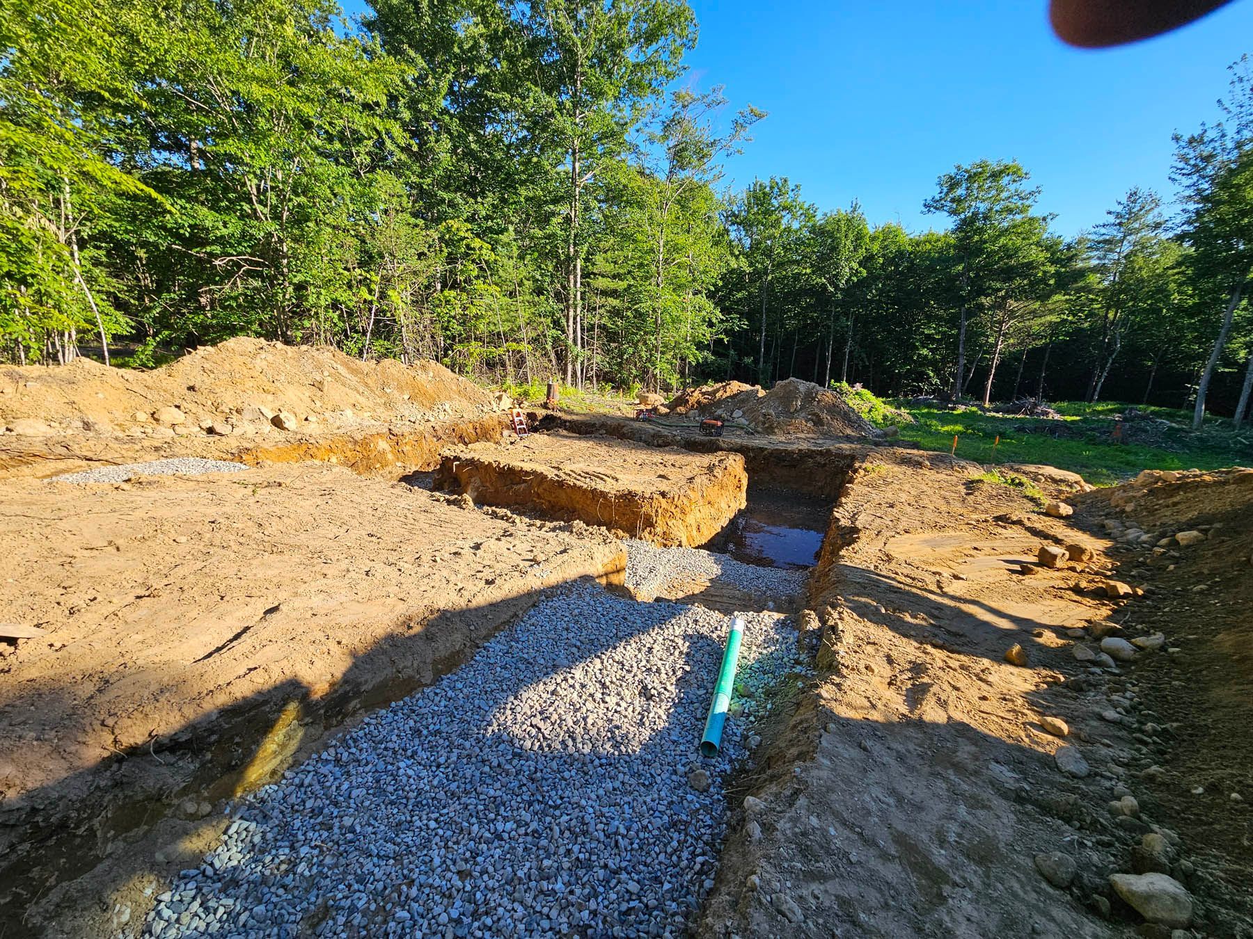 Excavated trench with gravel base for a construction project in a wooded area.