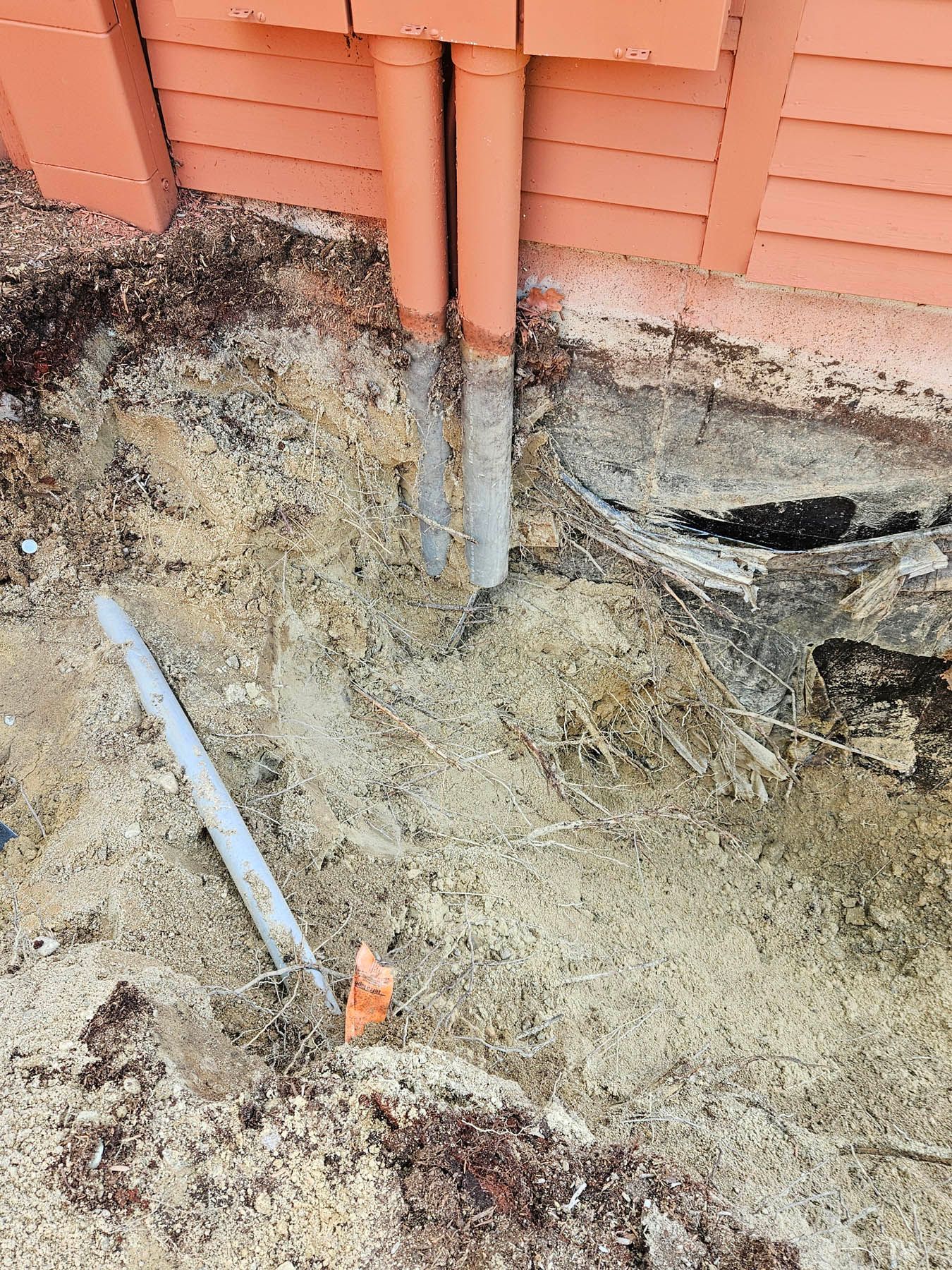 Pipes emerging from a brick building's foundation, surrounded by dirt and debris.
