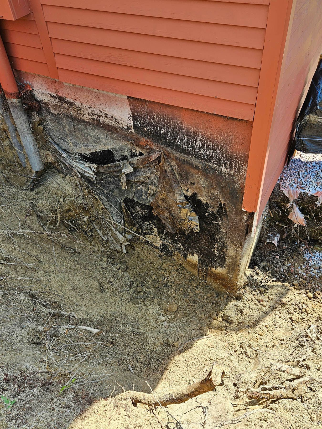 Rotting wood at the base of a red-sided building.  Brown and black damage is visible.