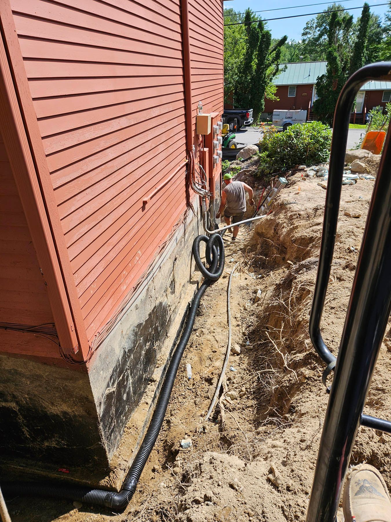 Black conduit runs underground next to a red building. Excavation in dirt.