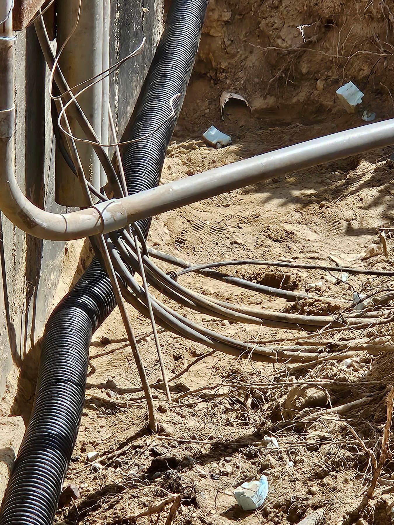 Black corrugated drain pipe and gray conduit against a foundation wall. Wires and exposed soil are visible.