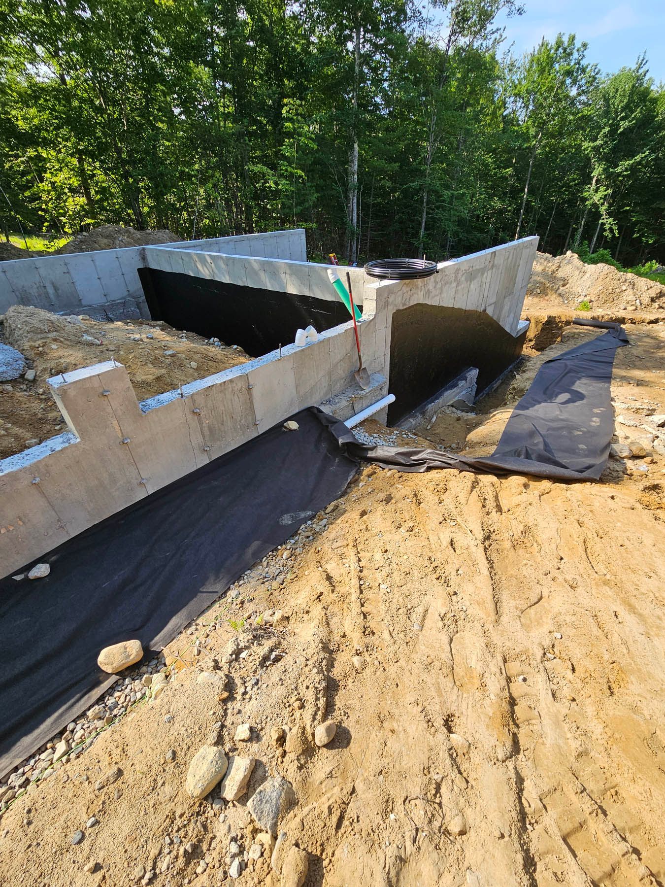 Concrete foundation of a building under construction with black waterproof membrane in a sandy area.