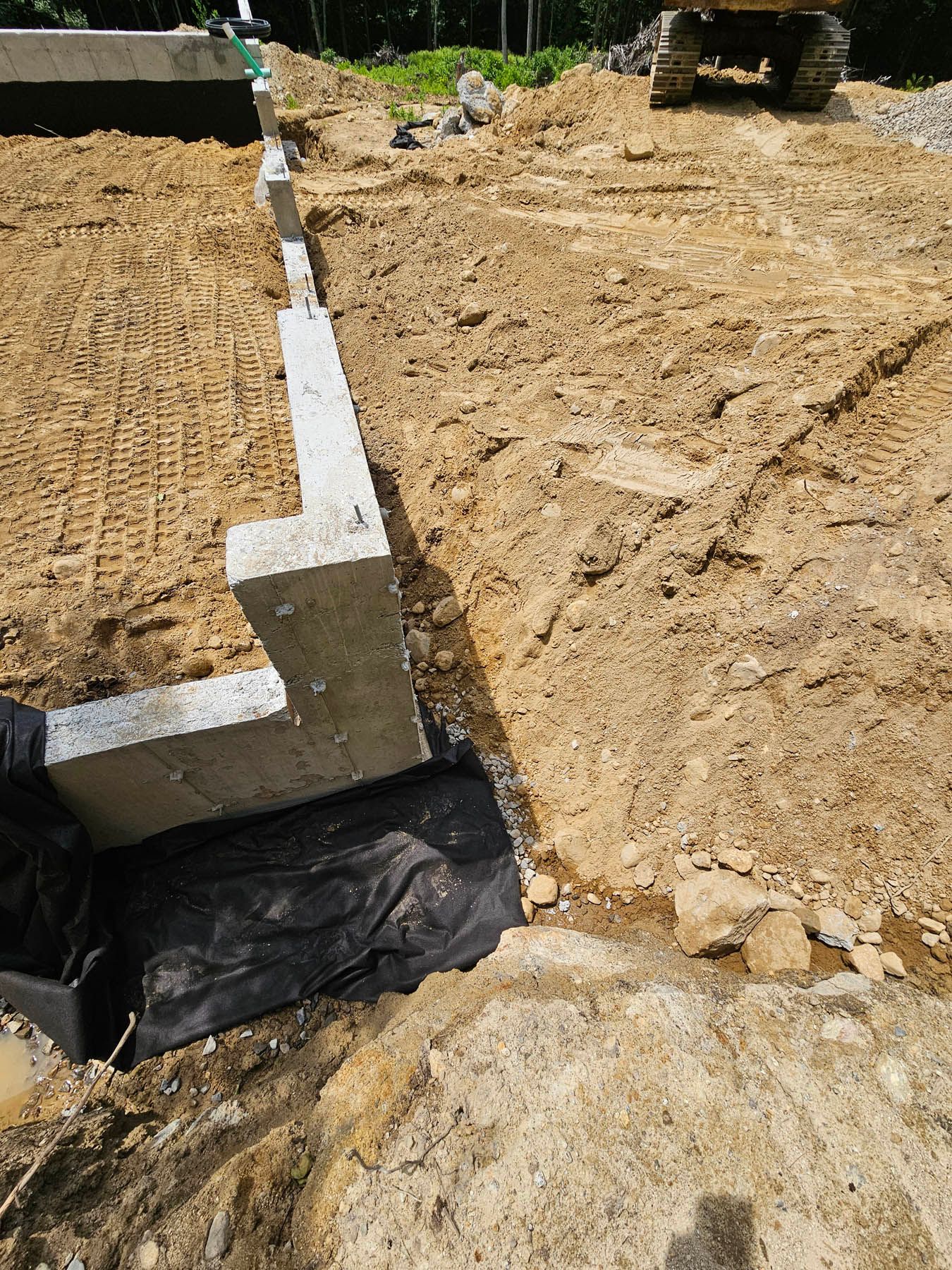 Concrete foundation being constructed in a dirt excavation, with an excavator in the background.