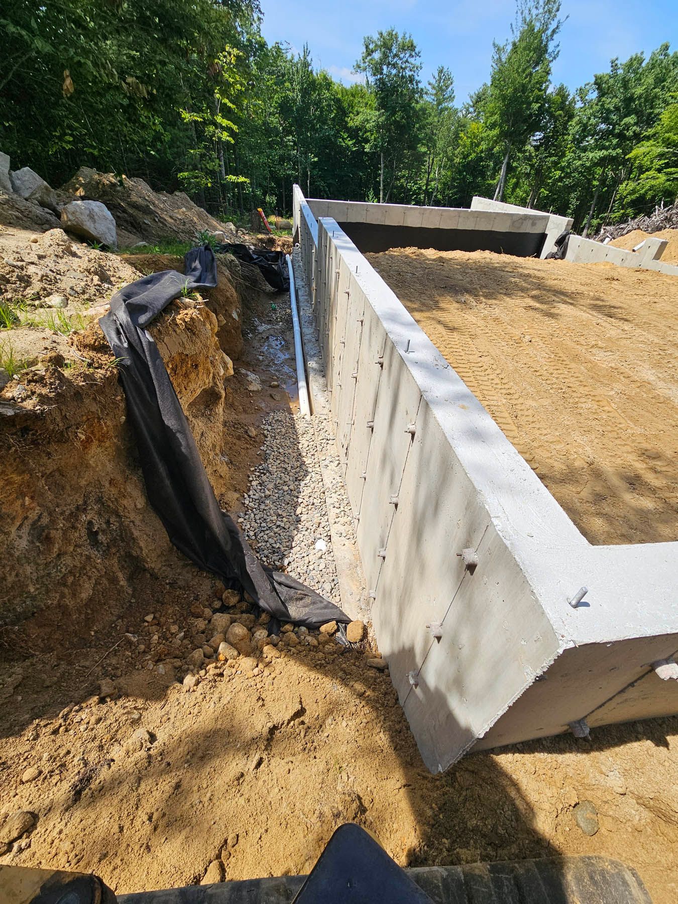 Concrete foundation wall with gravel drainage, dirt excavation, and black fabric.