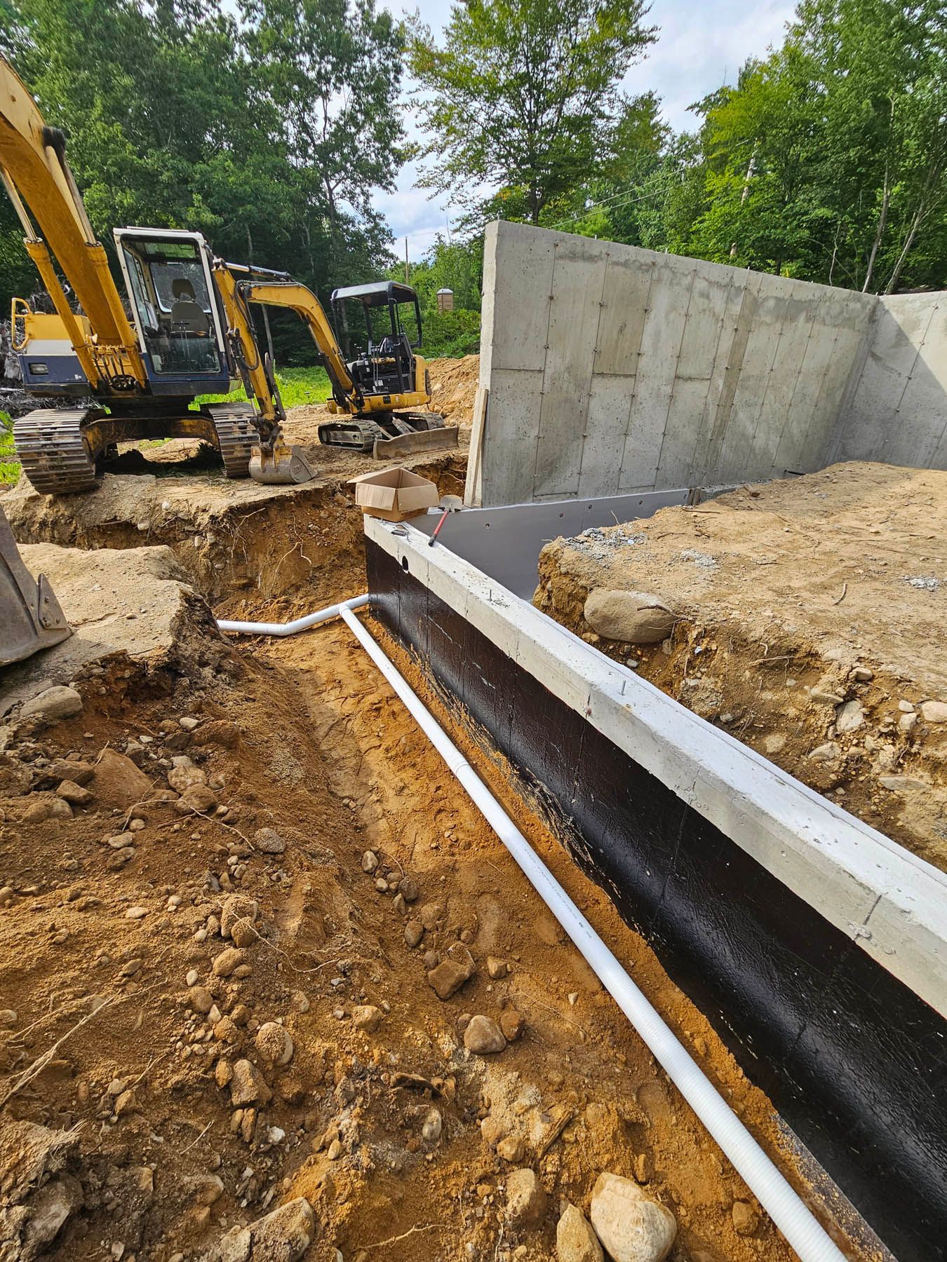 Construction site with excavators, concrete wall, and buried drainage pipes.
