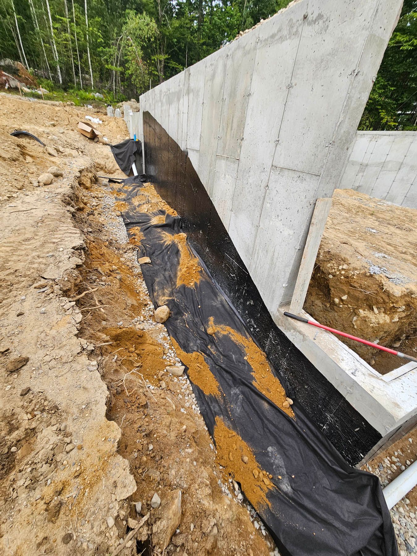 Concrete foundation wall with a black membrane, gravel, and dirt. Construction site.