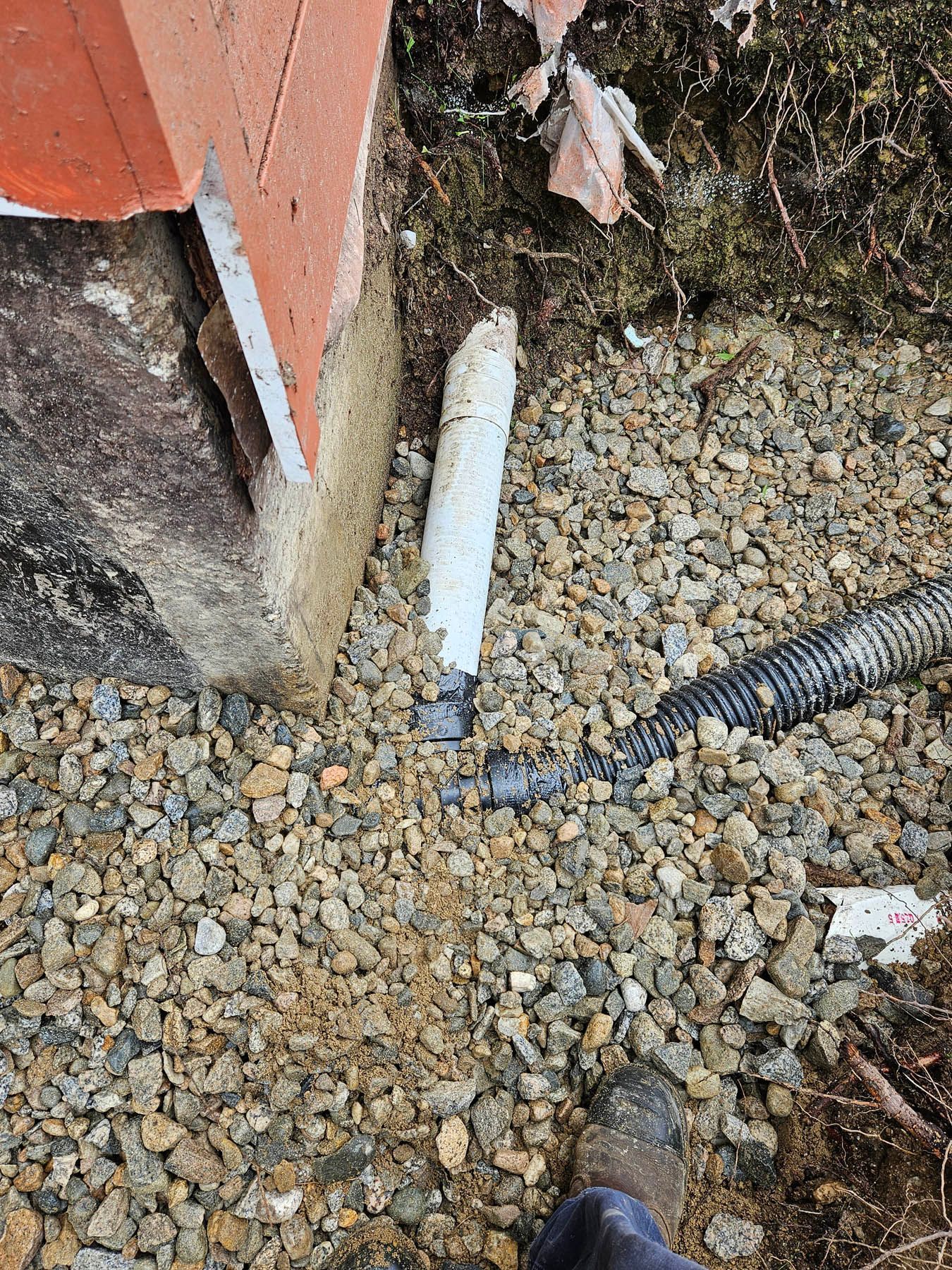Broken white pipe near foundation, gravel ground, and black corrugated hose.