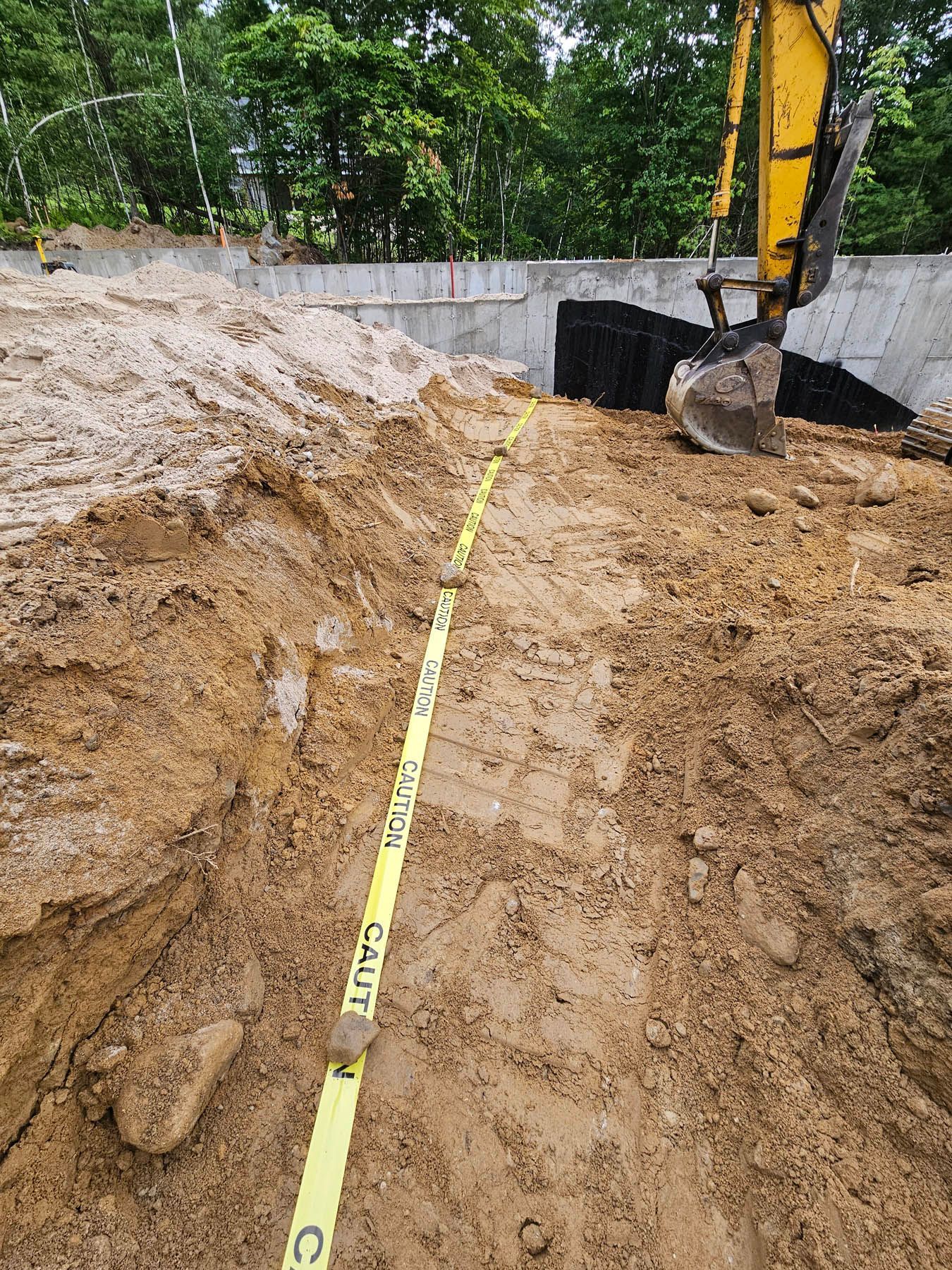 Construction site: Excavation trench with a yellow tape measure, next to a backhoe.