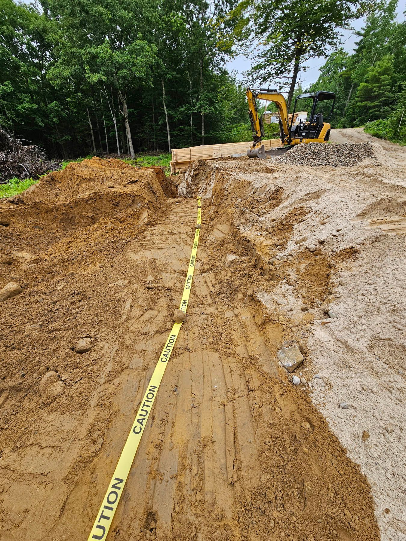 Construction site with dirt road, yellow caution tape, and excavator.