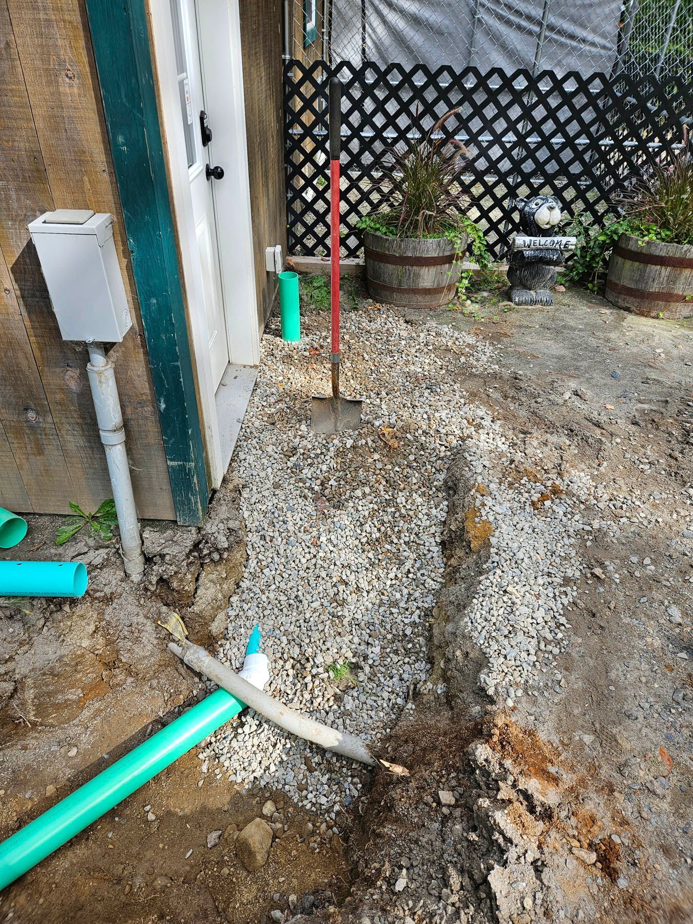 Gravel pathway being constructed next to a building. Green pipes and tools are visible.