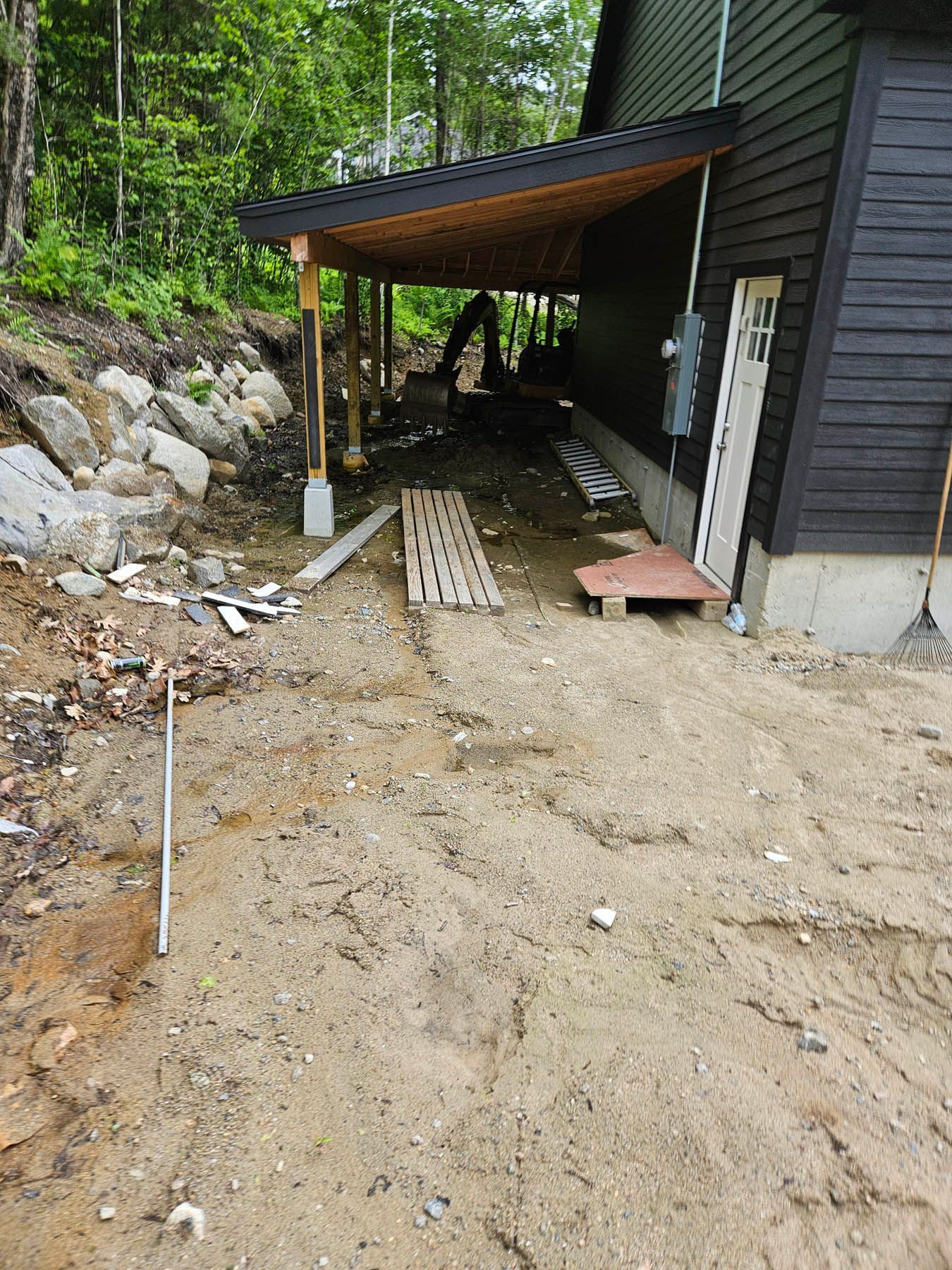 Dirt path leading to covered porch with construction materials near a dark house.