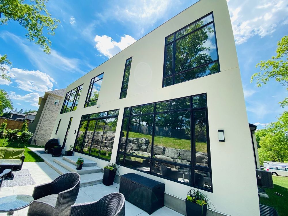 Modern white house with large black-framed windows and a patio on a sunny day.