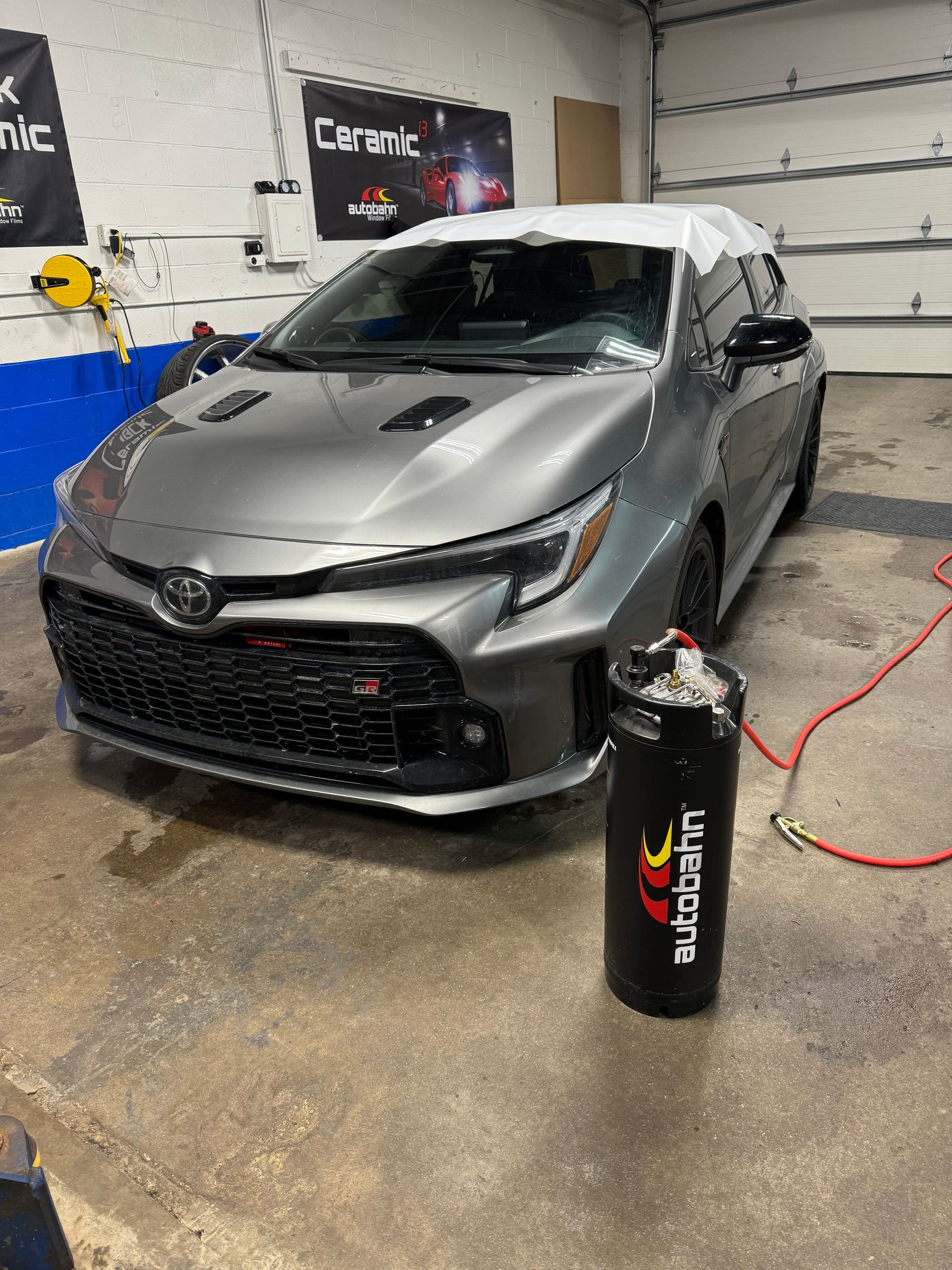 Grey Toyota GR Corolla in a garage, a black air tank is in front of it.