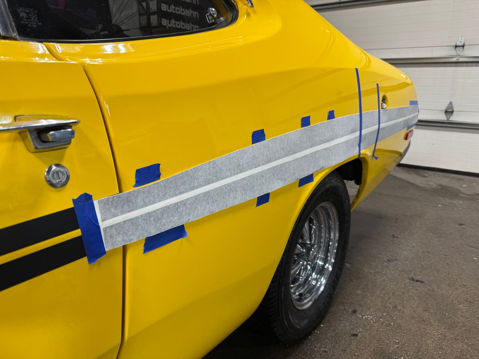 Yellow classic car with gray stripe taped on side, in a garage.