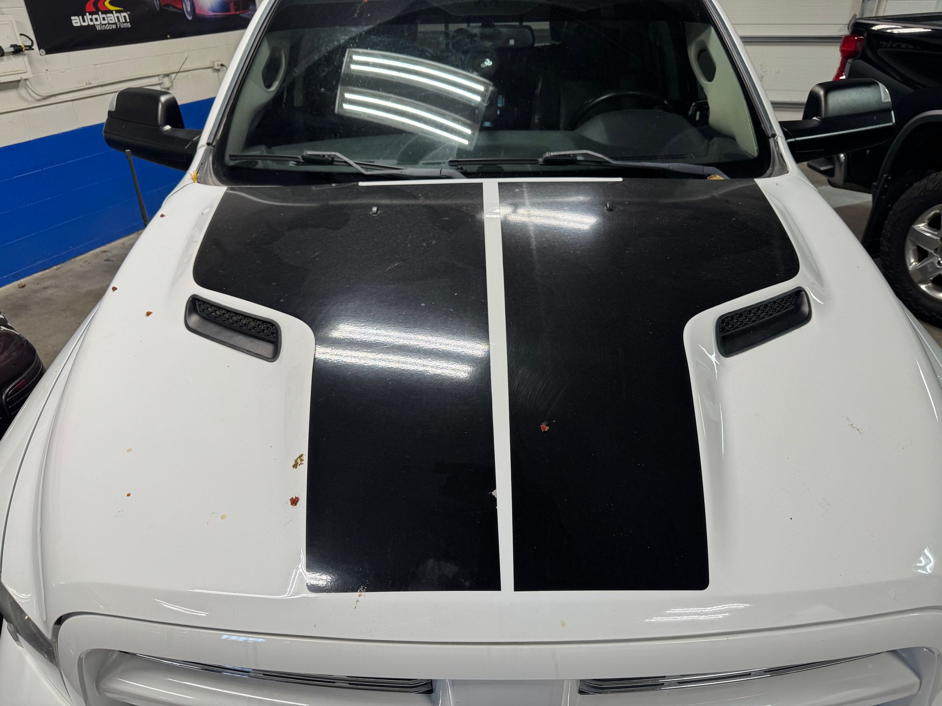 White truck with black hood stripe and vents, parked indoors.