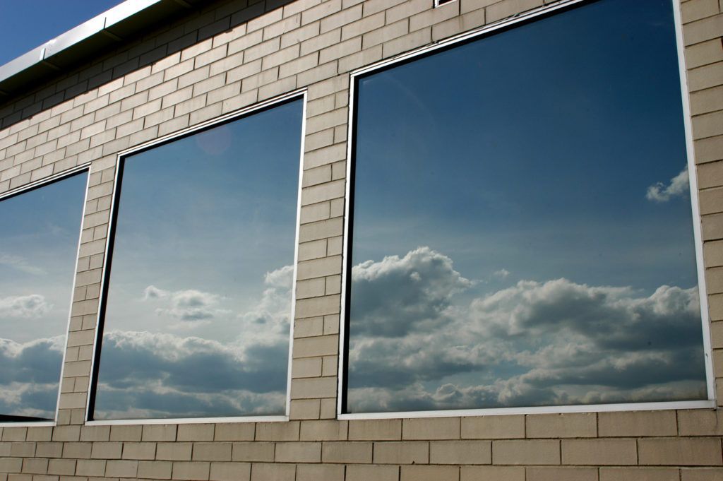 Three rectangular windows reflect a cloudy blue sky, set in a beige brick building.