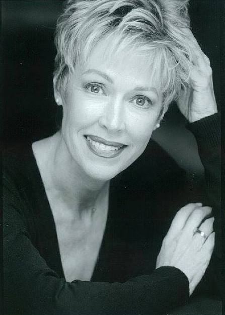 A black and white photo of a woman smiling with her hand in her hair.