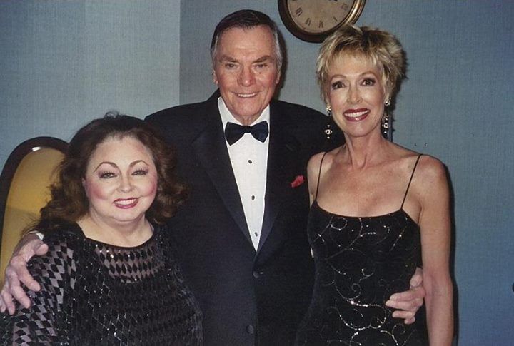 A man in a tuxedo and bow tie poses with two women