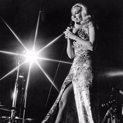 A woman in a long dress is singing into a microphone on a stage.