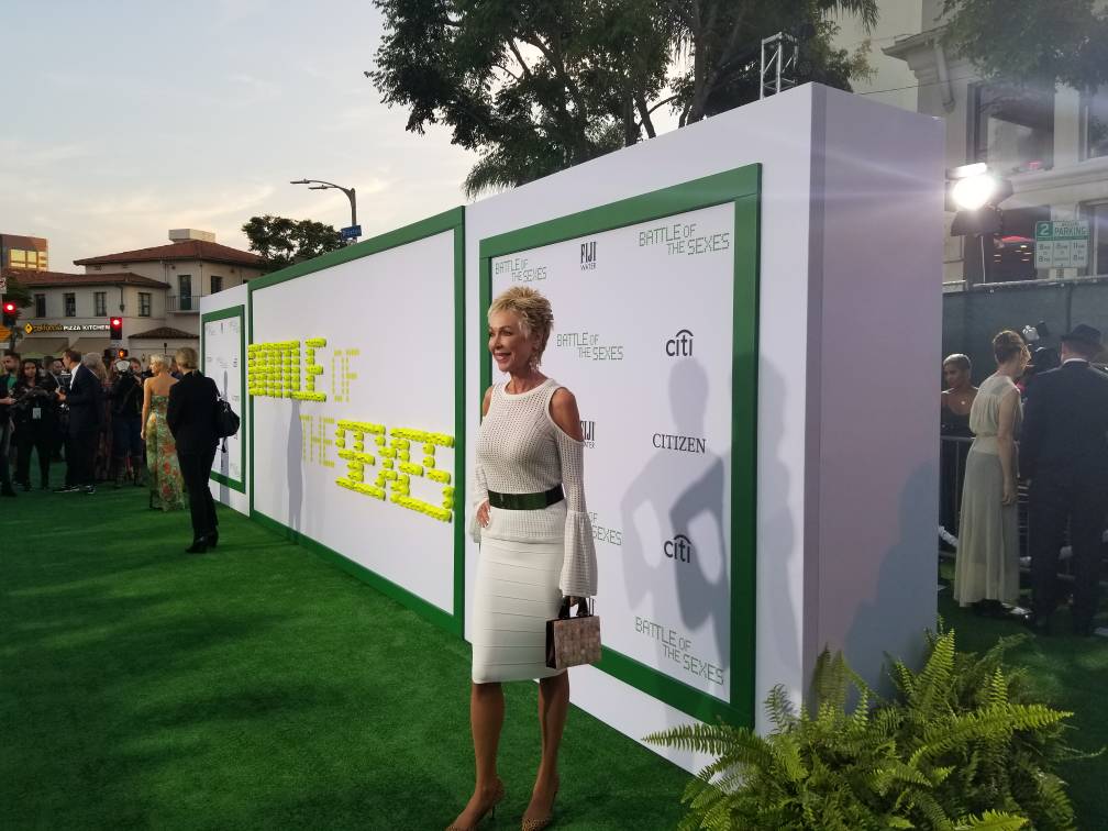 A woman in a white dress is standing in front of a wall.