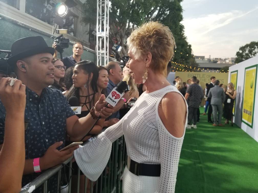 A woman is being interviewed with a microphone at a red carpet event.