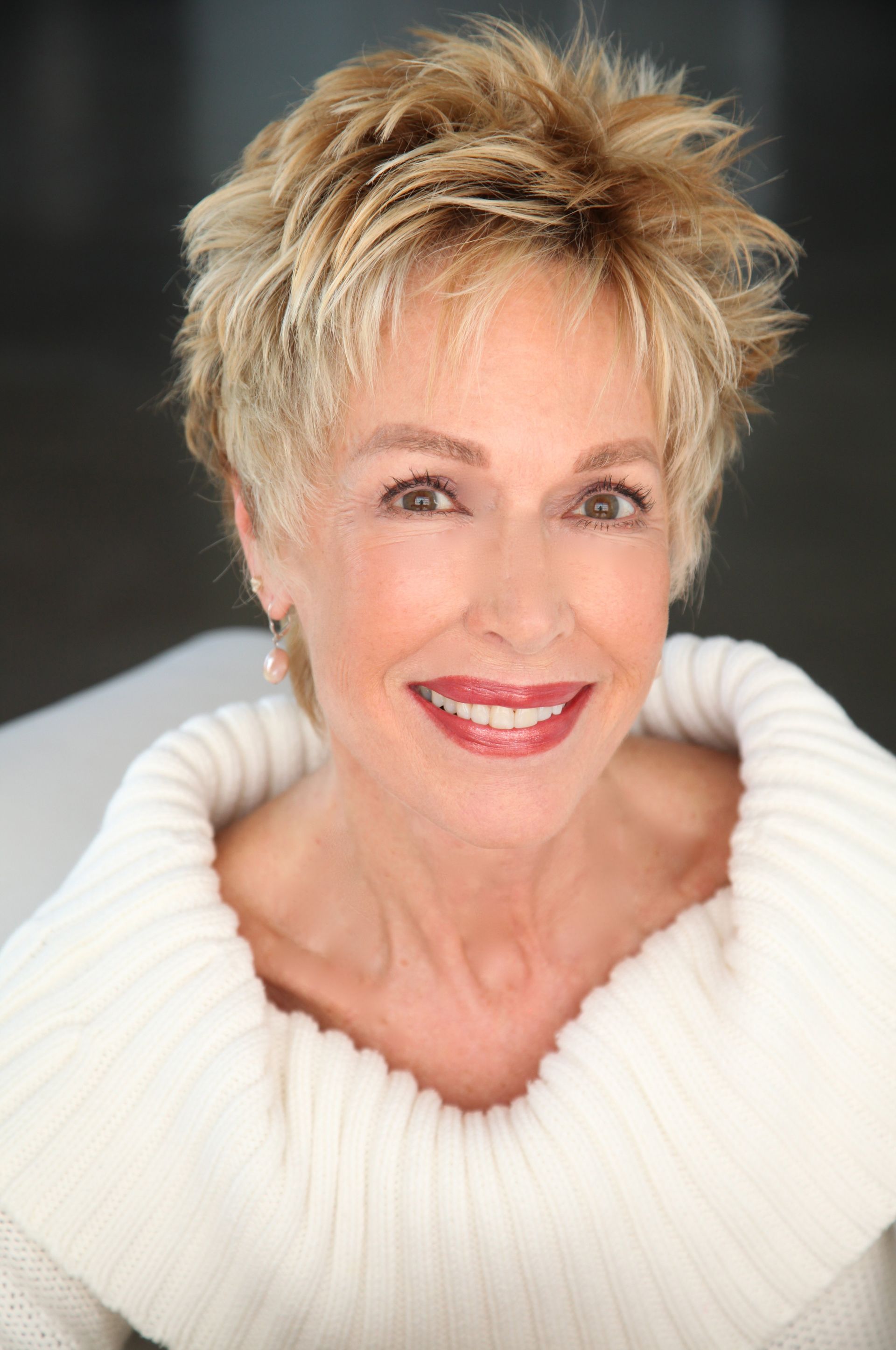 A woman is wearing a white sweater and smiling for the camera.