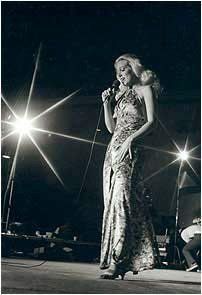 A woman in a long dress is singing into a microphone on a stage.
