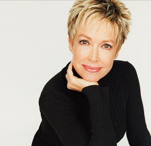 A woman in a black turtleneck is smiling with her hand on her chin