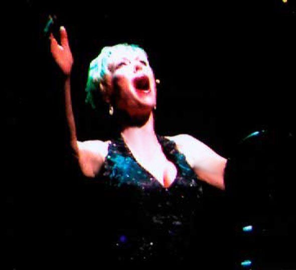 A woman with green hair is singing into a microphone on a stage.