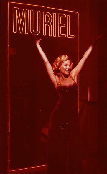 A woman is standing in front of a sign that says muriel.