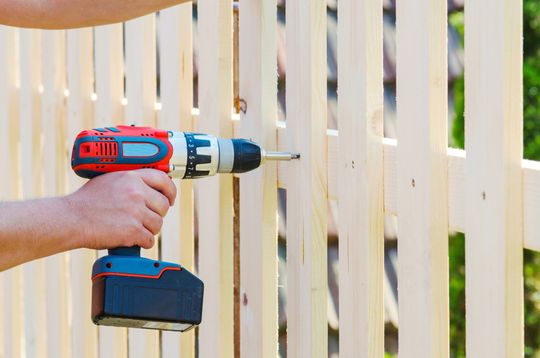 a person is using a drill on a wooden fence