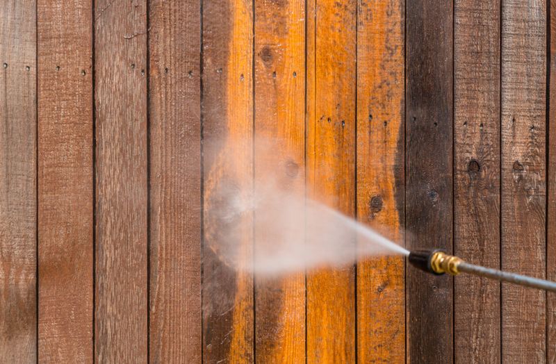 a person is cleaning a wooden fence with a high pressure washer