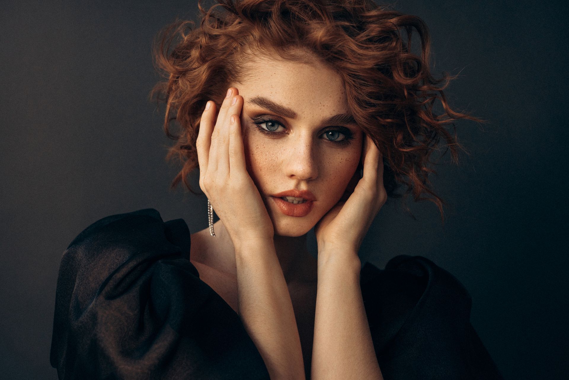 Una donna con lunghi capelli biondi e ondulati sorride, indossando una canotta bianca su uno sfondo beige.