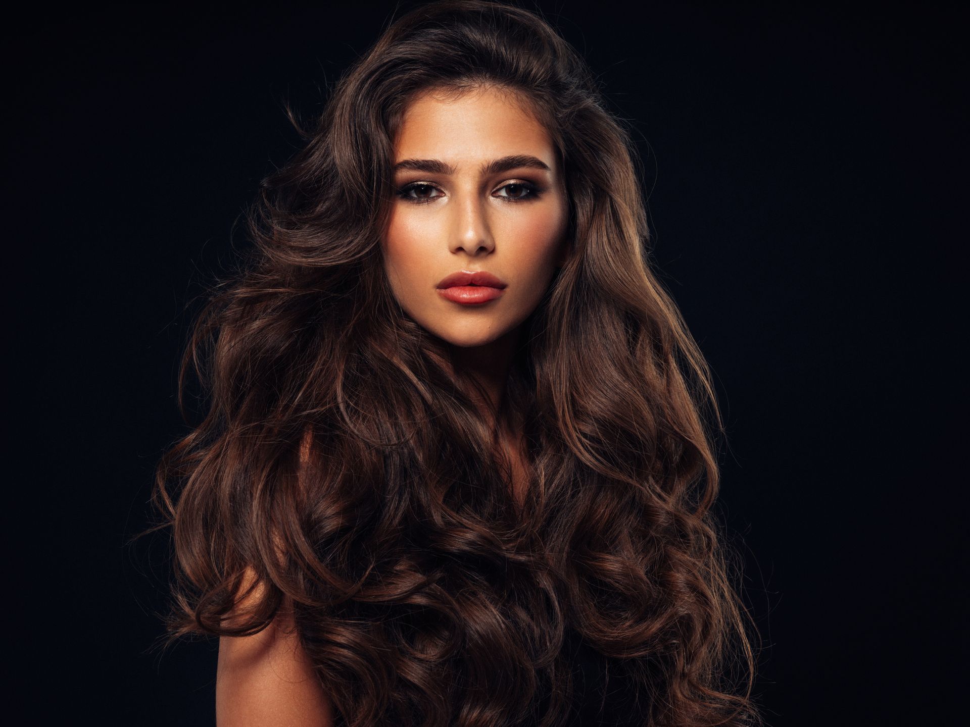 Donna con capelli castani ondulati, che indossa una canottiera rosa, che guarda oltre la spalla con un leggero sorriso.