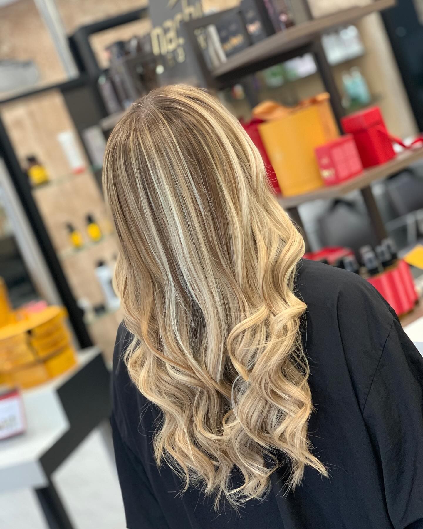 Donna con lunghi capelli biondi e castano chiaro, mossi e con mèches, in un salone di bellezza.