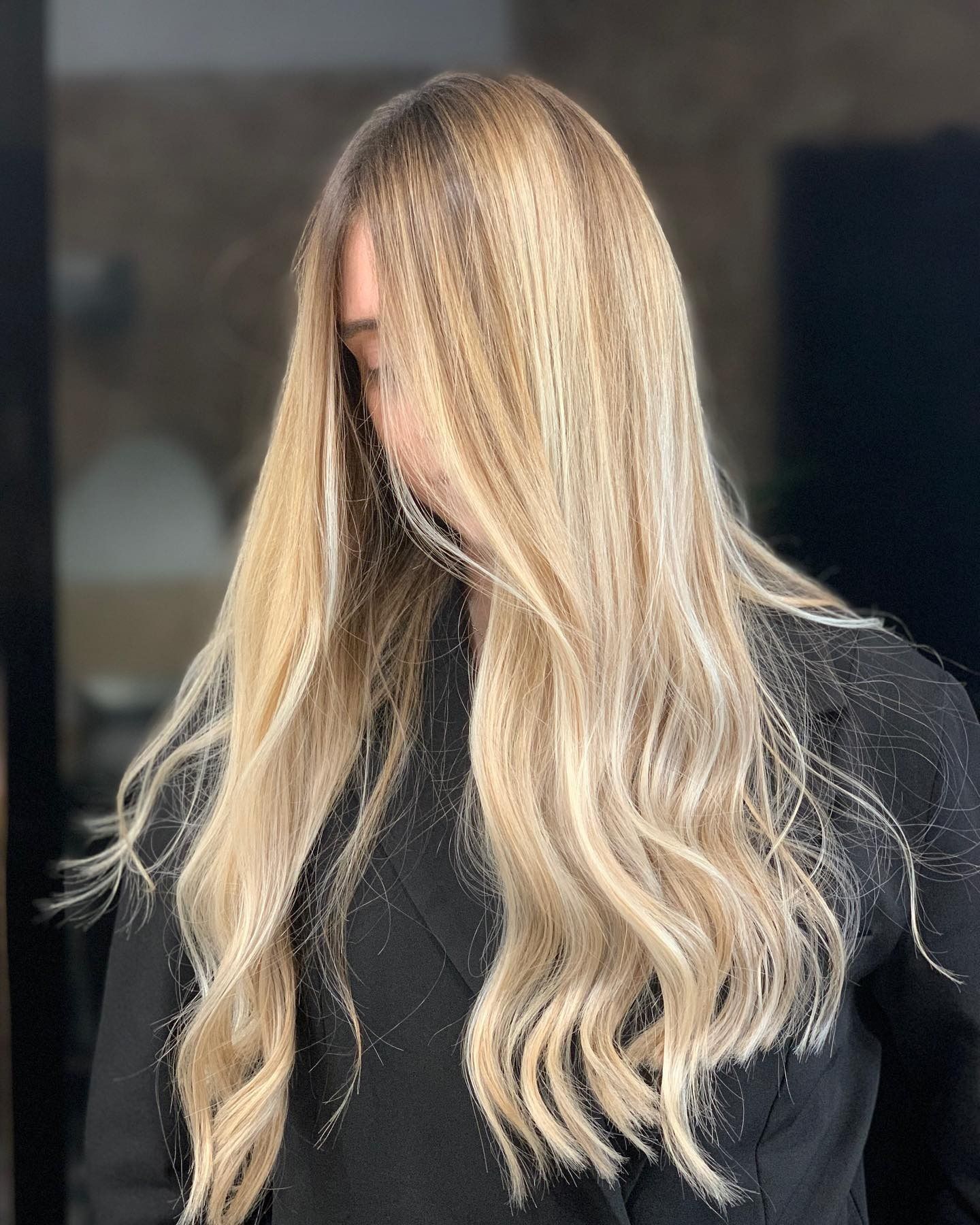 Donna con lunghi capelli biondi e ondulati; indossa un top scuro e tiene la testa bassa.