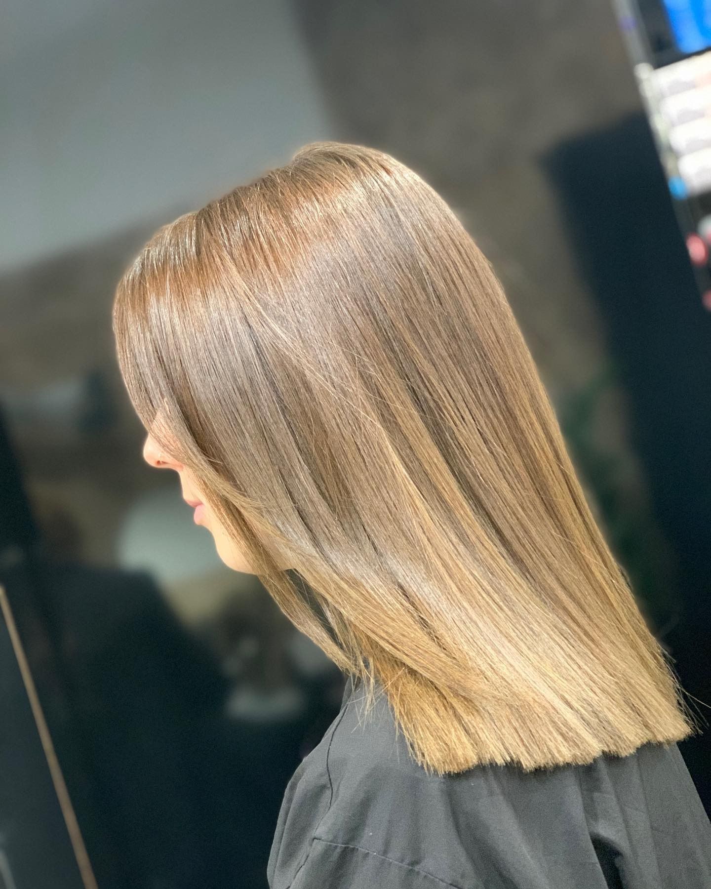 Donna con capelli lisci, biondi, lunghi fino al mento, taglio netto, con frangia, girata di lato in un salone.