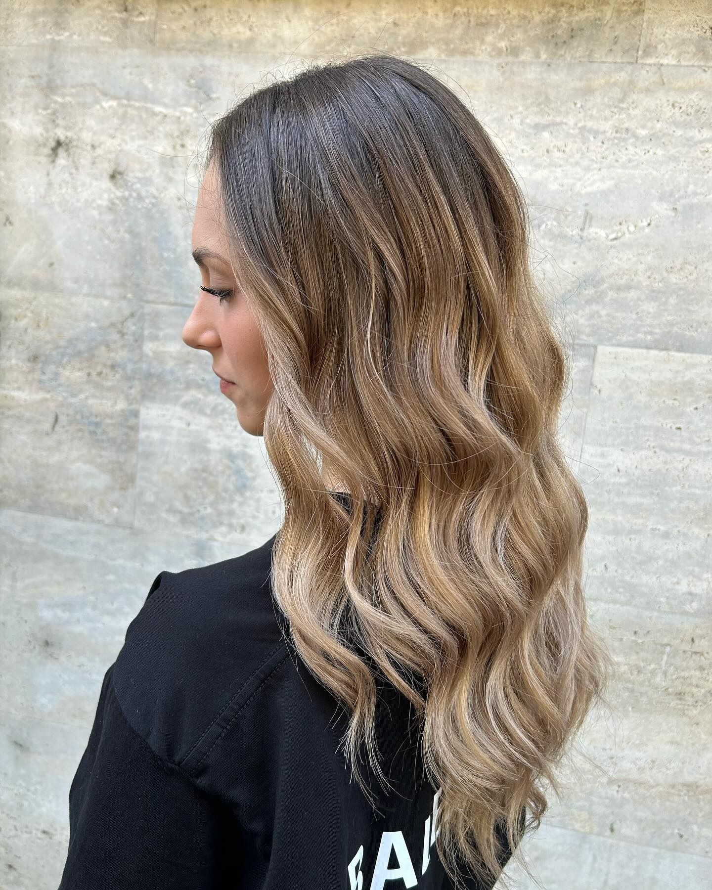 Donna con capelli mossi e sfumati, vista di profilo laterale, contro una parete neutra.