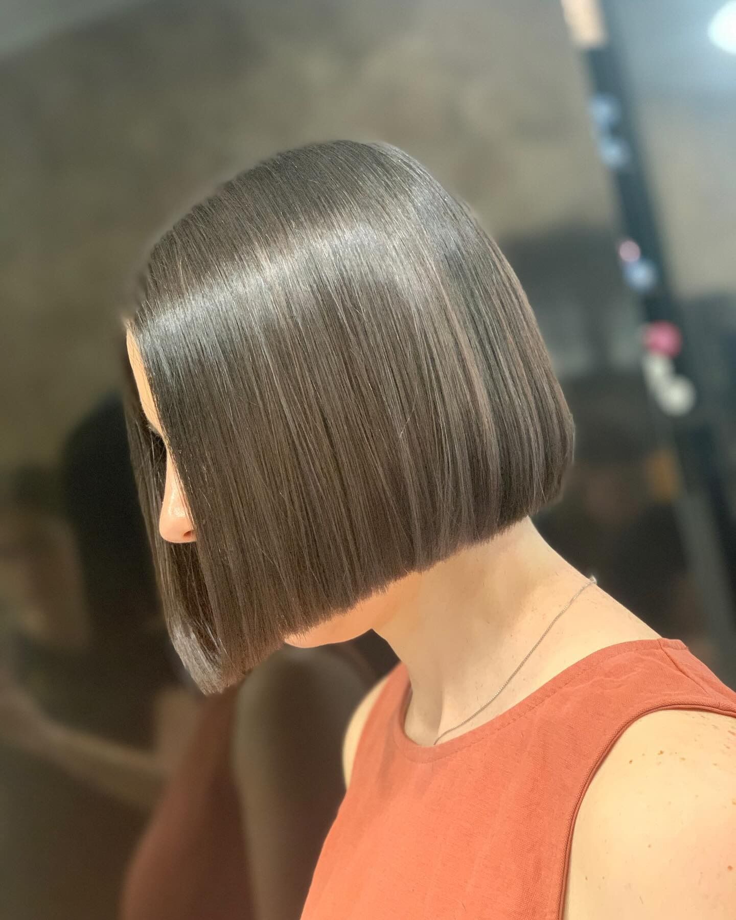 Donna con un elegante taglio di capelli castano scuro e un top color ruggine, in un salone di bellezza.