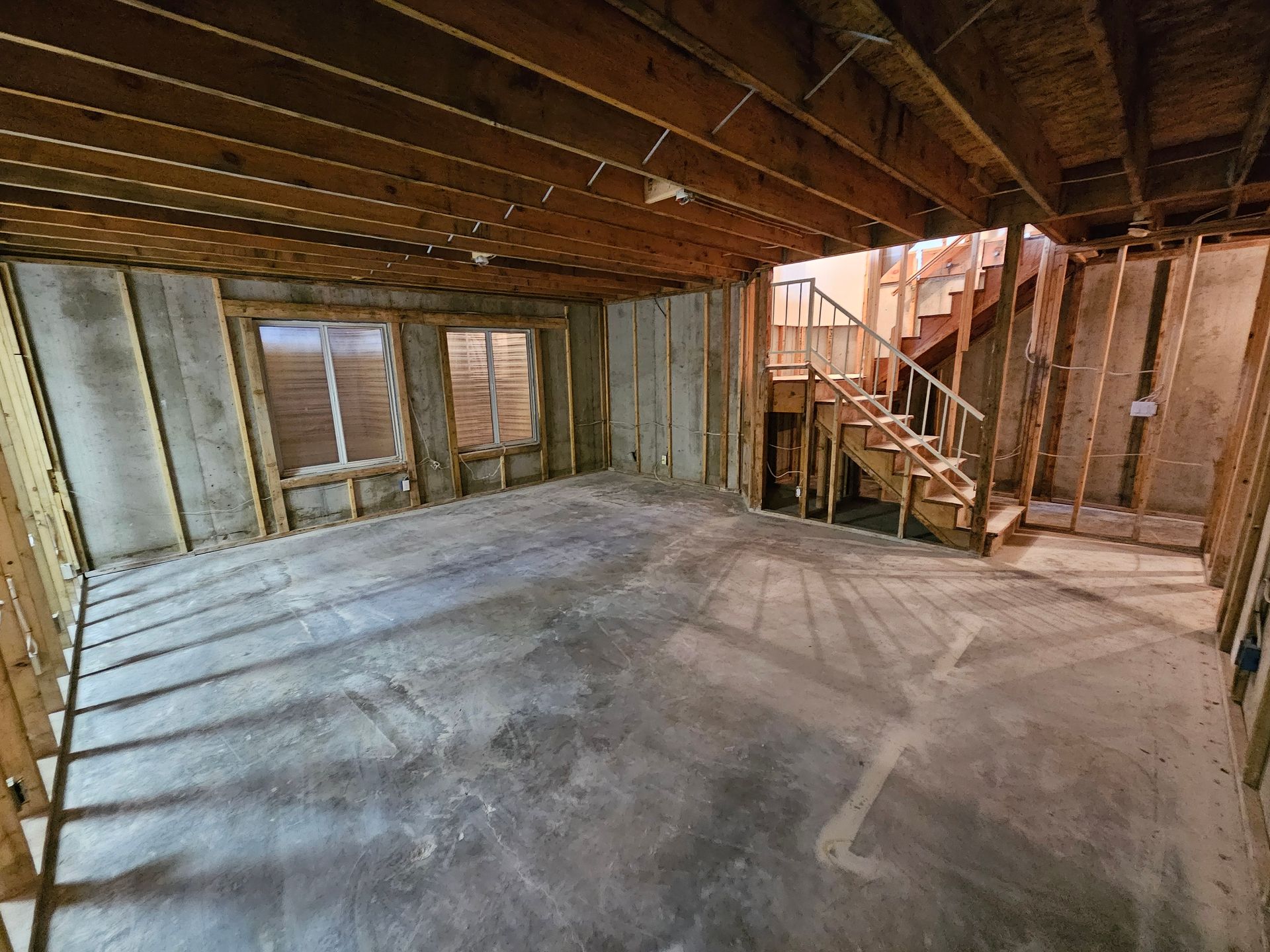 An empty basement with stairs and a wooden ceiling.