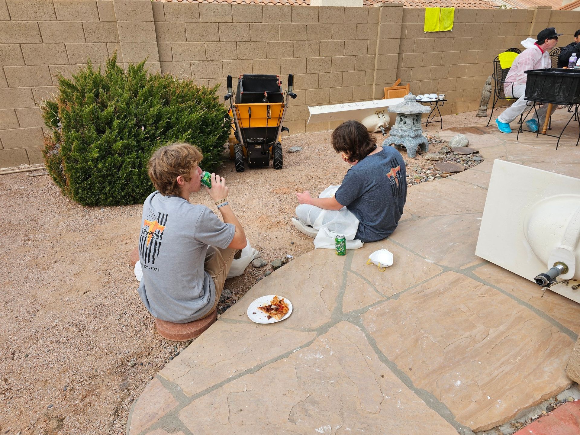 Two men are sitting on a patio eating pizza and drinking beer